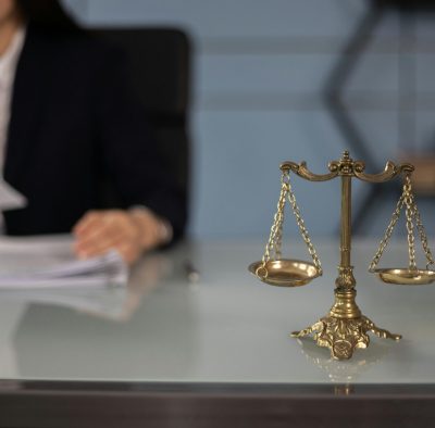 Balance scales on a desk in a professional office with a blurred businesswoman in the background.